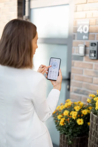 Mujer cierra la puerta o enciende la alarma de la casa con el teléfono — Foto de Stock