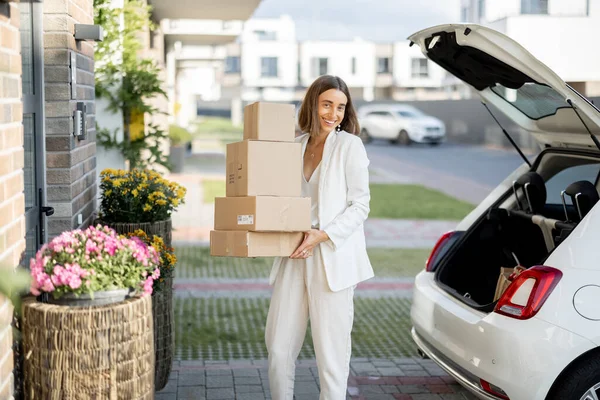 Mulher com um pacote perto de seu carro e casa — Fotografia de Stock