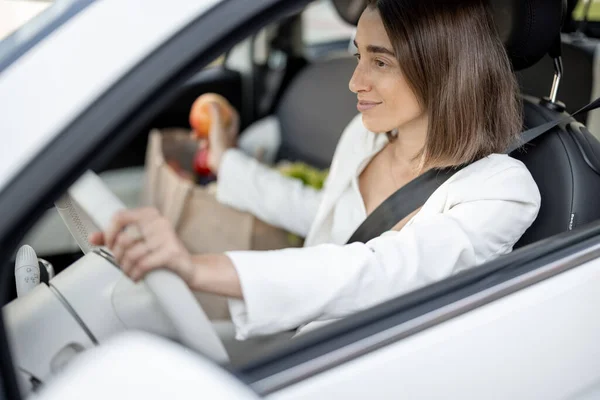 Mulher dirigindo carro com um saco de compras cheio de compras — Fotografia de Stock