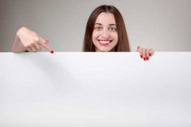 Studio gri arka plan üzerinde beyaz billboard işaret eden kadın