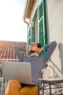Balkonda dizüstü bilgisayarlı bir adam var.