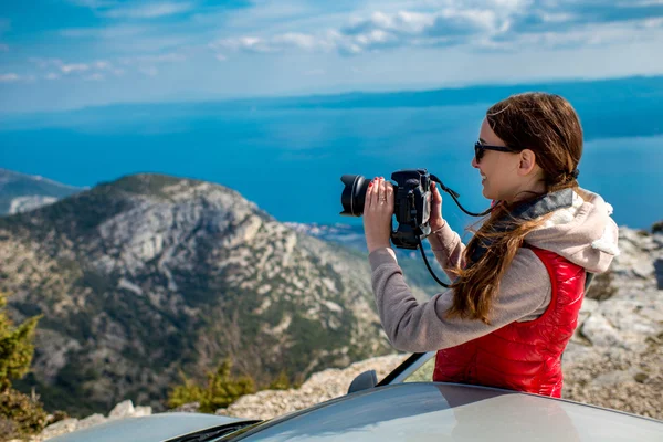 Vrouw fotograaf met auto op de bovenkant van berg — Stockfoto