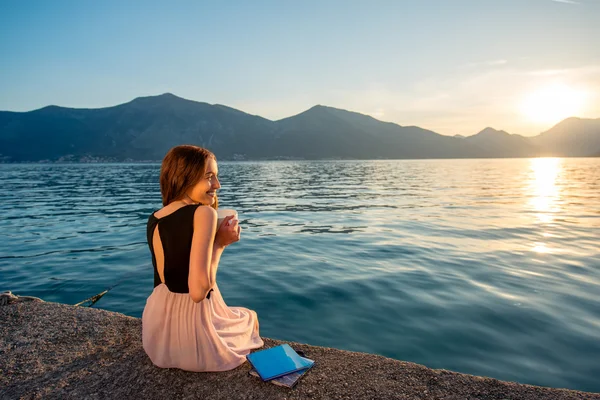 Young woman sitting on the pier at sunrise — Stock Photo, Image