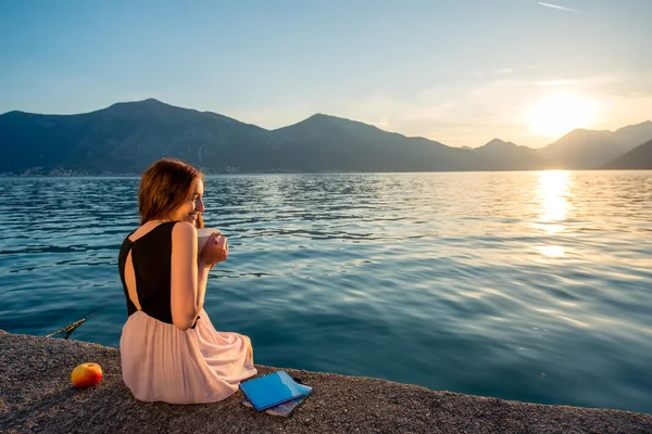 Young woman sitting on the pier at sunrise — Stock Photo, Image