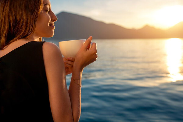 Young woman drinking coffee on the pier at sunrise
