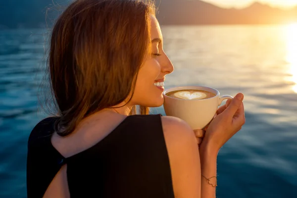 Young woman drinking coffee on the pier at sunrise