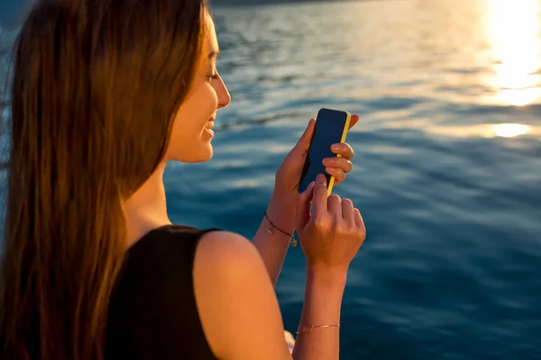 Güneş doğarken telefon kullanan genç kadın — Stok fotoğraf