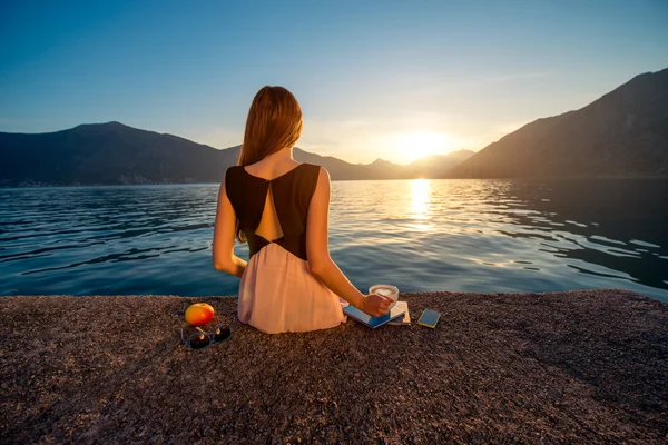 Young woman sitting on the pier at sunrise — Stock Photo, Image