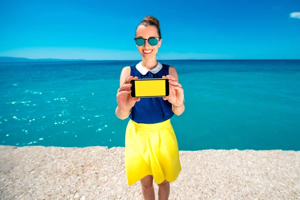 Женщина показывает экран телефона рядом с морем — стоковое фото