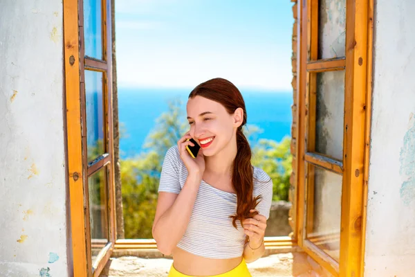 Vrouw met behulp van de telefoon in de buurt van het venster — Stockfoto