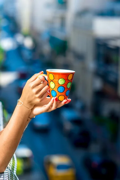 Sosteniendo taza de café de colores en el fondo borroso de la ciudad — Foto de Stock