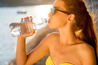 Woman drinking water from transparent bottle on the beach