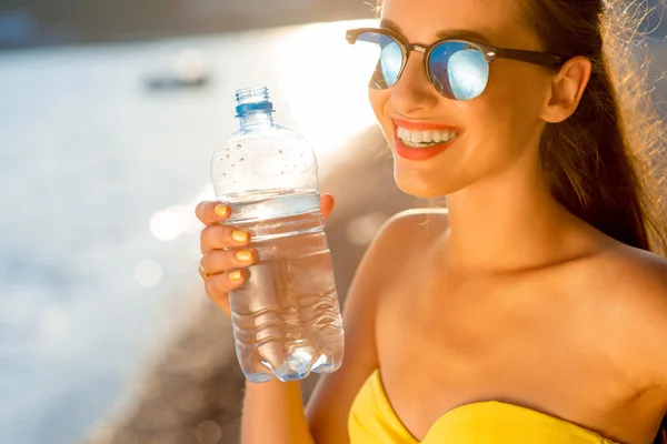 Donna che beve acqua dalla bottiglia trasparente sulla spiaggia — Foto Stock