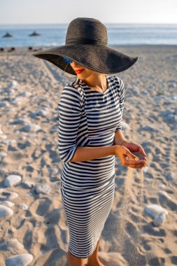 Woman in stripped dress with a hat on the beach