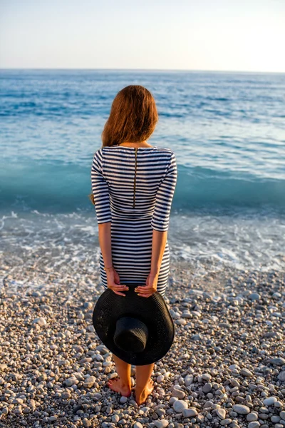 Woman in stripped dress with a hat on the beach — Stock Photo, Image