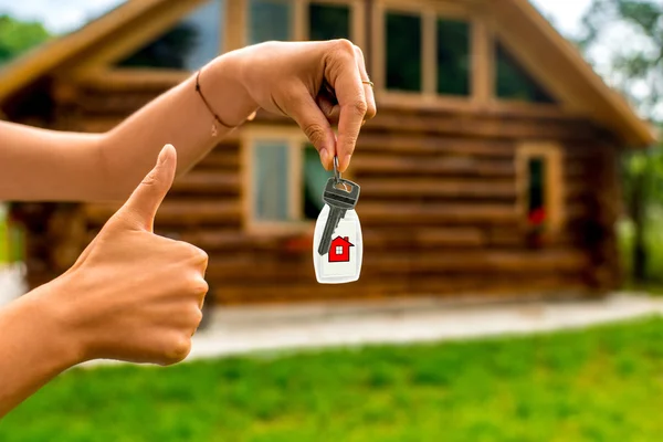 Holding house key with wooden cottage on background — Stock Photo, Image