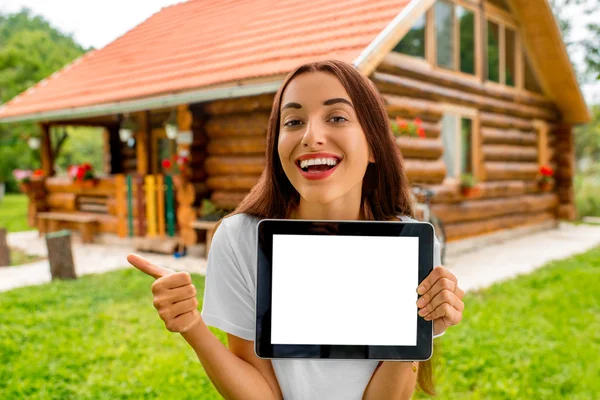 Žena zobrazeno digitální tabletu v blízkosti dřevěného domku. — Stock fotografie