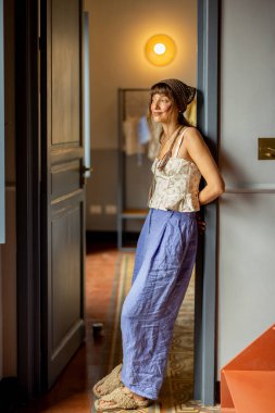 Sicilya 'da şık bir apartmanın kapısına dayanmış, rahat kıyafetler giymiş ve sakin bir Akdeniz sabahının tadını çıkaran bir kadın. Yavaş yaşam tarzı havası