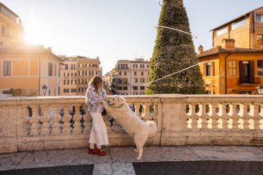 Kadın, Roma 'da İspanyol Merdivenleri' nin yanındaki süslü Noel ağacının yanında köpeğiyle şenlikli bir an yaşıyor. Tatil atmosferi, kış turizmi, yeni yıl ruhu, neşeli seyahat ve Avrupa yaşam tarzı