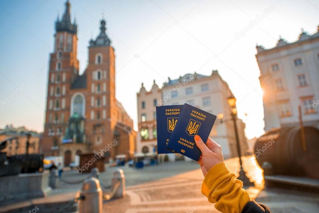 Female hands holding Ukrainian abroad passports on the Krakow city center background
