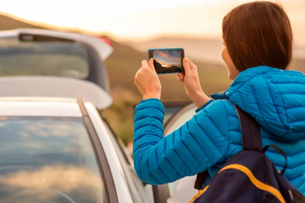 Viajera fotografiando la salida del sol con smartphon cerca del coche — Foto de Stock