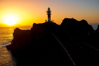 Deniz feneri günbatımı üzerinde kayalık sahil şeridine