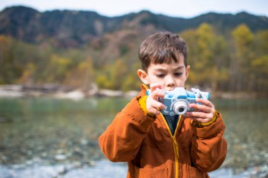 Bir çocuk, melez bir Brezilyalı ve japon güzel bir gölün önündeki fotoğraflara bakıyor. Bu bir turist gezisi..