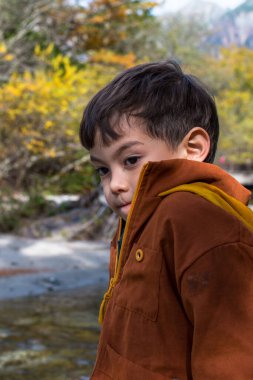 Ulusal parkta serüven sırasında, gölün berrak sularına bakan soğuk hisseden bir çocuğun dikey resmi.