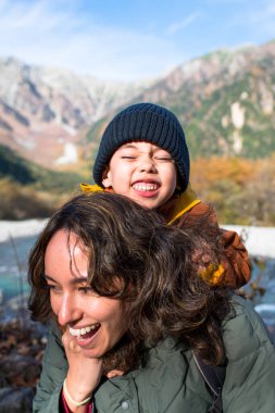 Oğul annesine sarılıyor, gezginlere gülüyor. Güz mevsiminde, güzel bir arazide, nehirler ve dağlarla birlikte.
