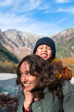 Sonbahar mevsiminde, güzel bir arazide, nehirler ve dağlarla dolu bir arazide, annesinin ve yolcuların sarıldığı dikey bir portre.