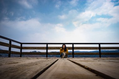 young girl sitting at wood bridge with cloudy sky from low angle leading line and space for text