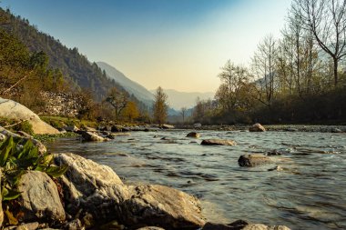 Yoğun ormanlar ve mavi gökyüzü ile kaplı sisli dağ vadisinden akan nehir şafak vakti Shergaon Arunachal Pradesh Hindistan 'da görüntülenir..