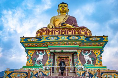 Büyük Buda Altın Heykeli 'nin yanında duran ve akşam karamsar gökyüzü olan kız dev Buda heykeli Tawang Arunachal Pradesh Hindistan' da çekilmiştir..