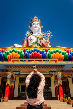 Budist renkli tanrıça heykelinin önünde dua eden genç kız sabah mavi gökyüzü ile birlikte Lumla taradevi manastırı Tawang Arunachal Pradesh Hindistan 'da çekilmiştir..