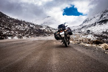 Arka planda kar örtüsü dağları olan ıssız bir yolda motosikletli araç Tawang Arunachal Pradesh 'te çekiliyor..