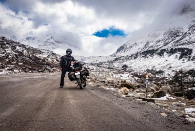 Dişlileri dolu bir motosikletle ıssız bir yolda ve karla kaplı dağlarda tek başına gezen adam sela pass tawang arunachal pradesh 'te görüntülenir..
