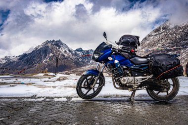 Arka planda kar örtüsü dağları olan ıssız bir yolda motosikletli araç Tawang Arunachal Pradesh 'te çekiliyor..
