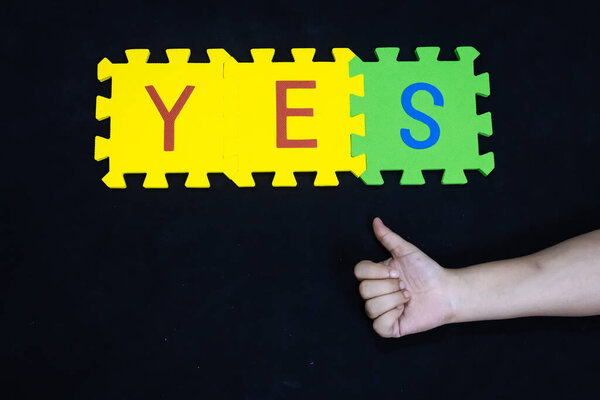thumbs up sign over foam puzzle spelling yes for communication and acceptance concept