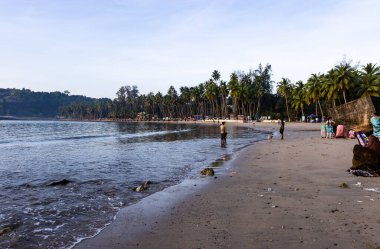 Palmiye ağaçları ve yürüyen insanlarla kaplı Andaman adalarındaki deniz kıyıları 18 Eylül 2024 tarihinde Corbyns Cove Beach, Andaman ve Nicobar Adası 'ndaki liman Blair, Hindistan' da çekilmiştir..