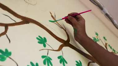 El kaplaması boya fırçası ve yeşil yaprak tasarımı ile duvar sanatı oluşturuyor.
