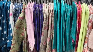 Moda mağazasındaki elbise raflarında renkli kadınlar ve etnik kurtiler sergileniyor