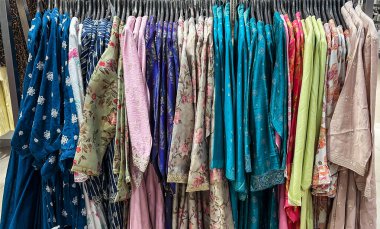 Moda dükkanındaki elbise raflarında renkli kadınlar ve etnik kurtiler sergileniyor