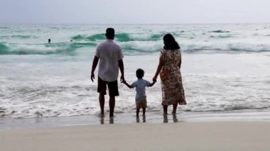 Çocuklar plajda ellerini tutarak okyanus dalgalarına bakıyor. Manzaranın tadını çıkarıyorlar. Radhanagar Sahili 'nde çekiliyor..