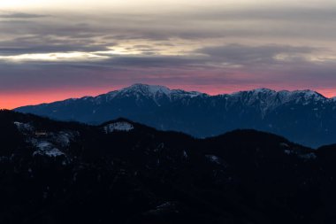 Pembe ve turuncu akşam gökyüzü altında dramatik dağ siluetleri