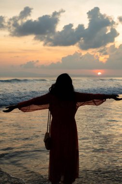 Okyanus esintisini kucaklayan kadın silueti ile huzurlu sahil gün batımı