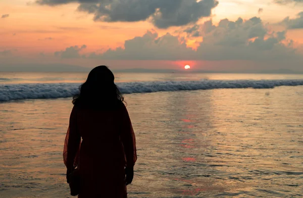 Gün batımında okyanus dalgalarında kolları açık duran siluet kadın.