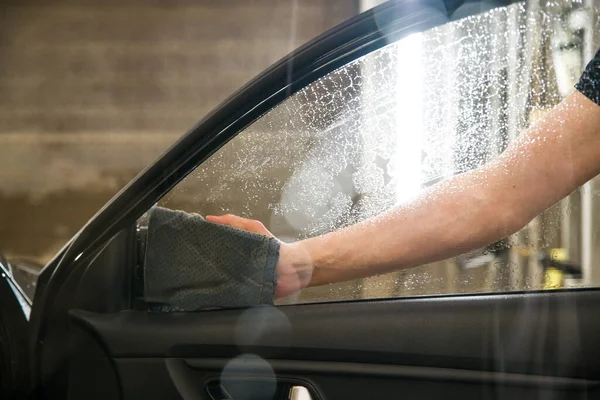 Mano con gamuza falsa limpia el vidrio de la puerta del coche — Foto de Stock