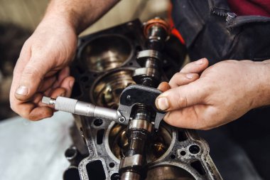 Eldeki bir ölçüm cihazı, bir arabanın arka planına karşı, derin bir alan derinliğindeki kam milini ölçer.