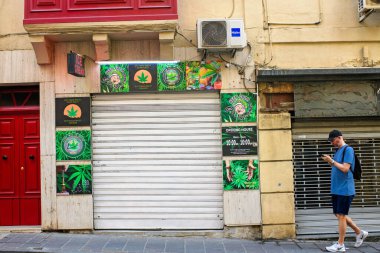 Sliema, Malta - 11.03.2025: Kenevir temalı tabelalı kapalı CBD mağazası ve kenar mahallede yürüyen bir adam.