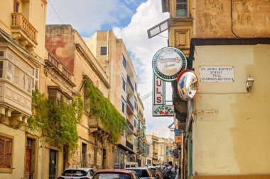 Sliema, Malta - 11.03.2025: Kireçtaşı binaları, balkonları, tırmanma tesisleri, eski tabelaları ve köşesinde konveks güvenlik aynası olan geleneksel Malta caddesi.
